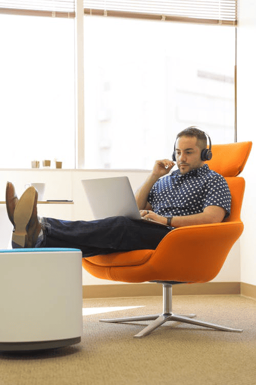 man sitting in orange lounge chair using laptop working a hybrid work schedule